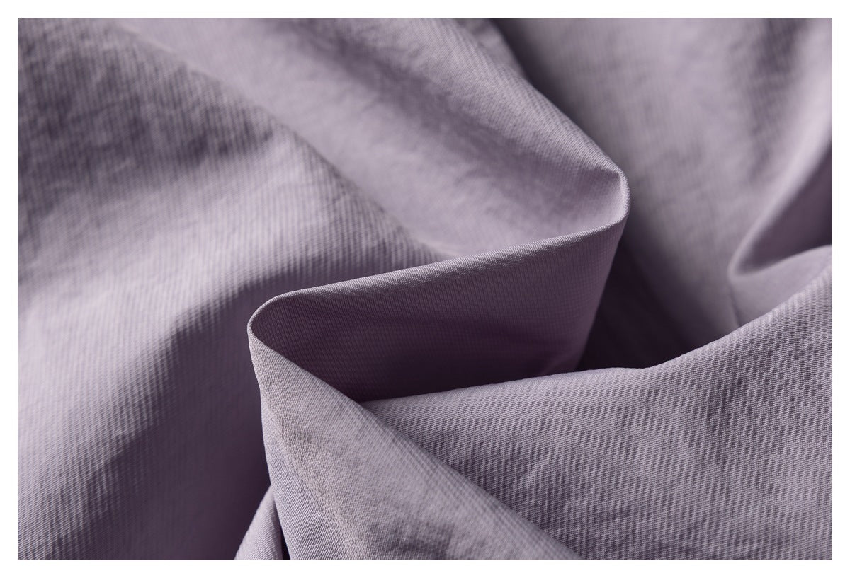 Close-up of folded lavender-gray fabric showing its fine woven texture and subtle tonal pattern.