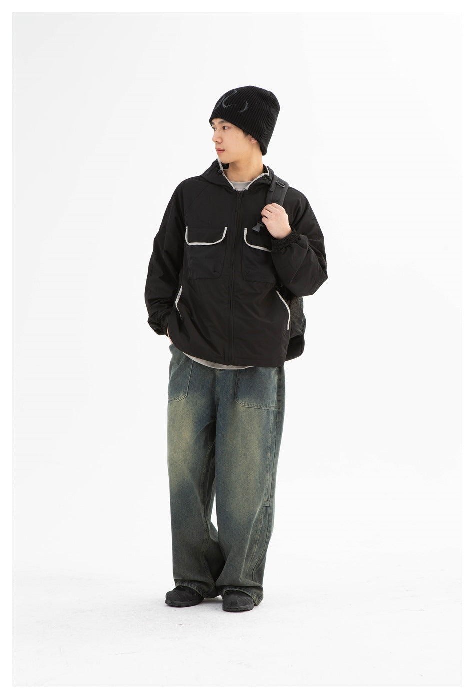 Man wearing a black hooded jacket with white-trimmed pockets, shown at a slight angle.