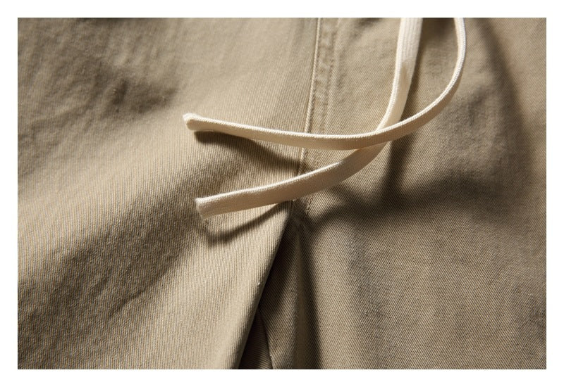 Close-up of the light drawstrings crossing over the khaki trouser fabric.