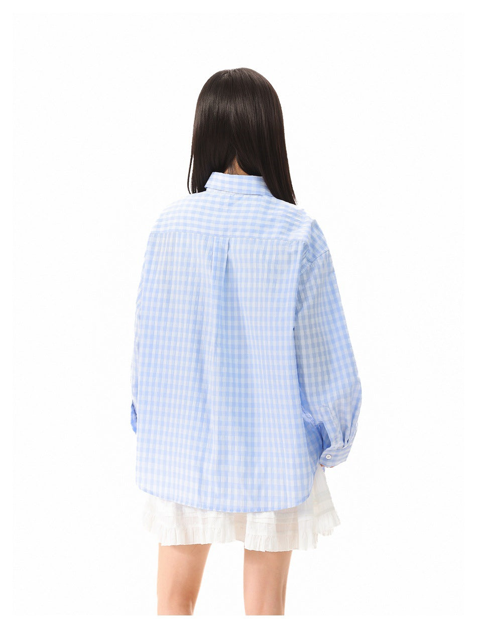 Model seen from behind wearing an oversized pale blue and white gingham shirt with white ruffled shorts.