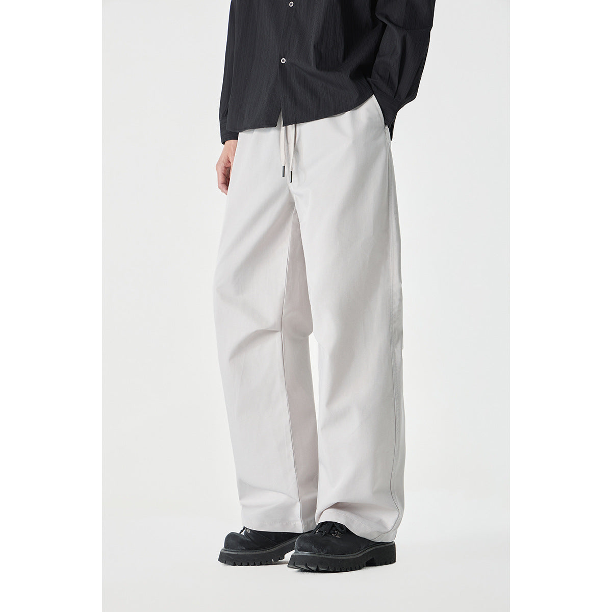 Cropped model wearing loose, light gray wide-leg drawstring pants with a black shirt and black shoes.