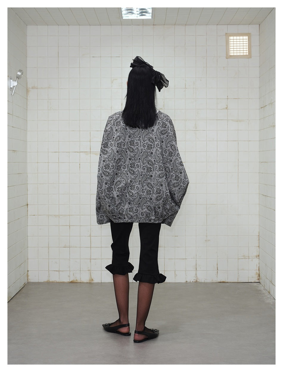 Back view of a model wearing an oversized gray paisley jacket with black cropped ruffle-hem pants.