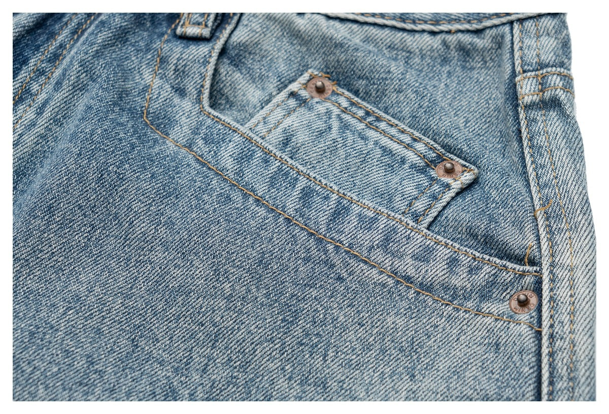 Close-up of a faded blue denim pocket with tan stitching and bronze rivets.