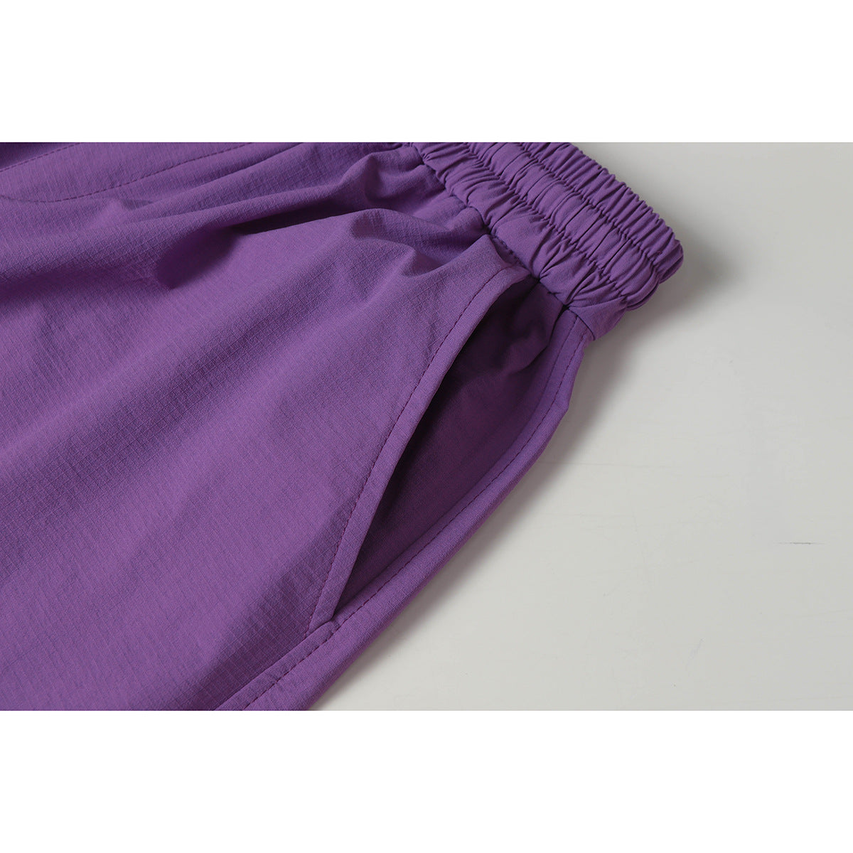 Close-up of purple pants showing the gathered elastic waistband and side pocket opening.
