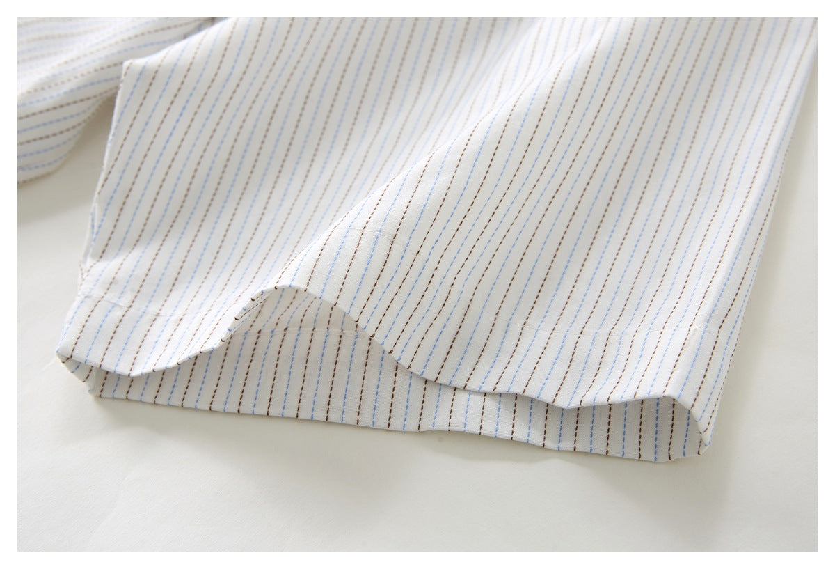 Close-up of the curved hem on a white shirt with fine blue and brown stripes.