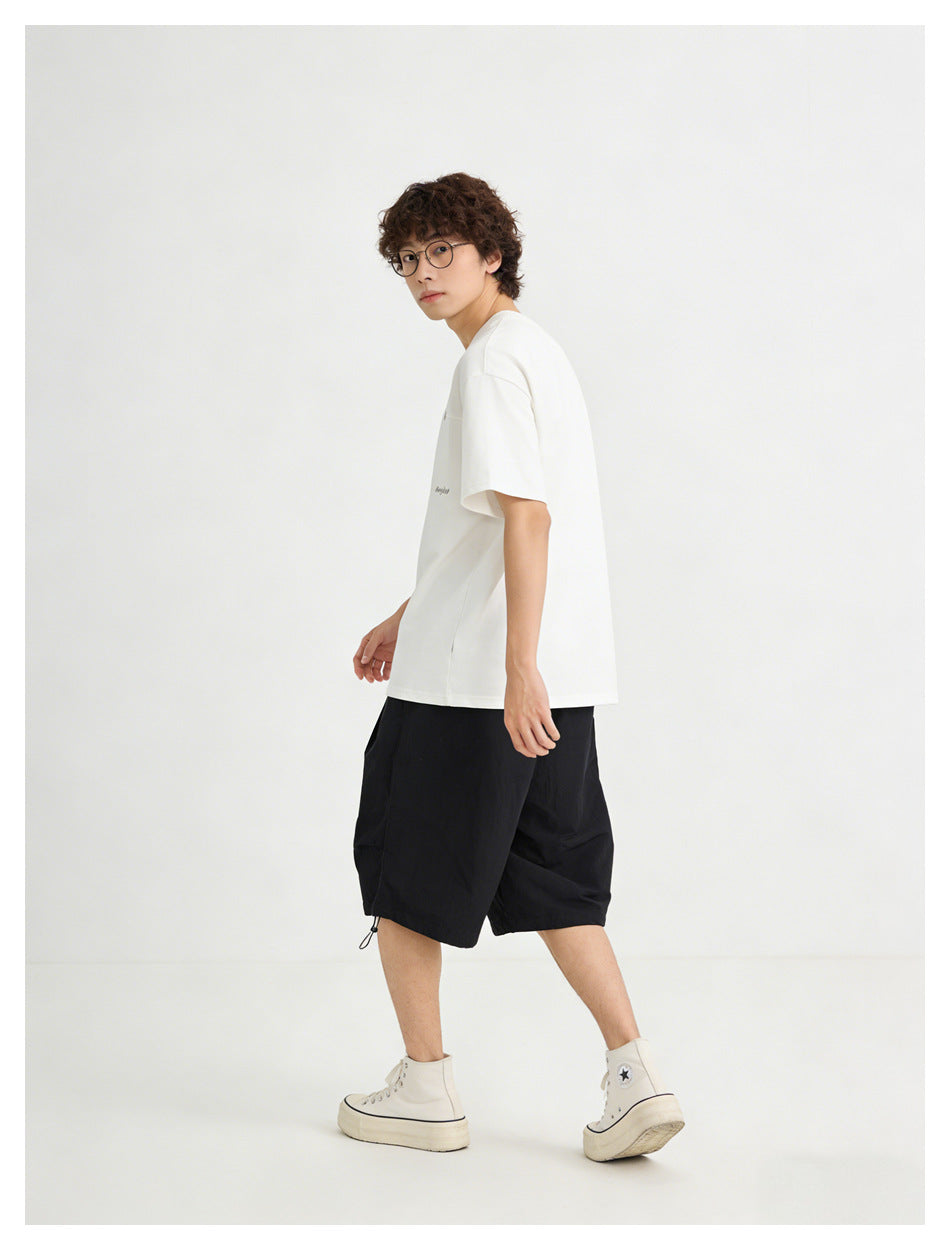 Model wearing a white short-sleeve T-shirt with tiny dark chest lettering and black shorts, shown in profile.