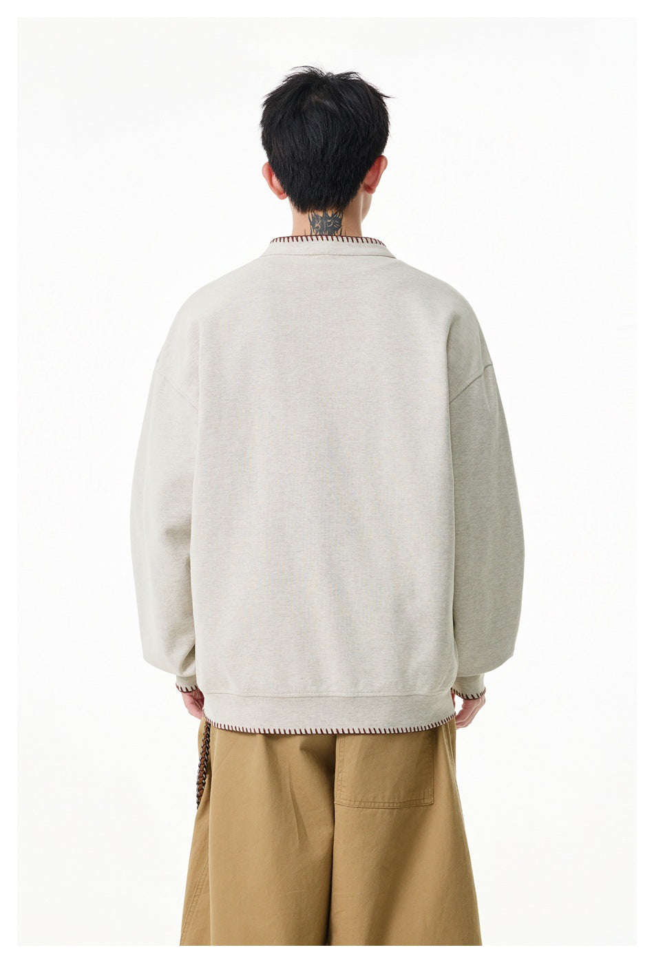 Back view of a man wearing a cream pullover with contrast stitching at the collar, cuffs, and hem.