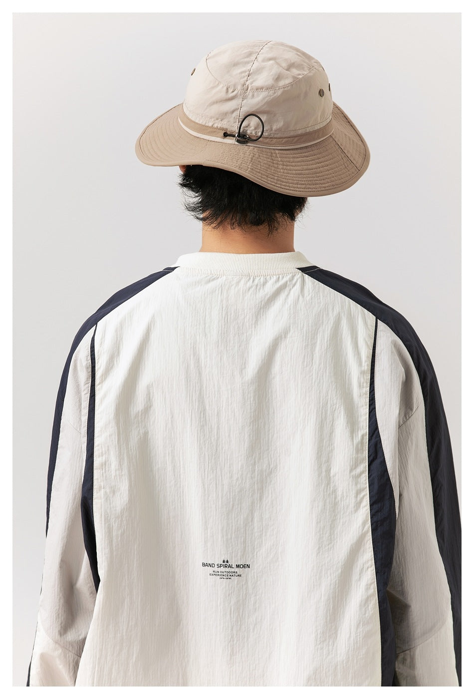 Back view of a model wearing an ivory pullover with navy sleeve panels and a small printed graphic near the hem.