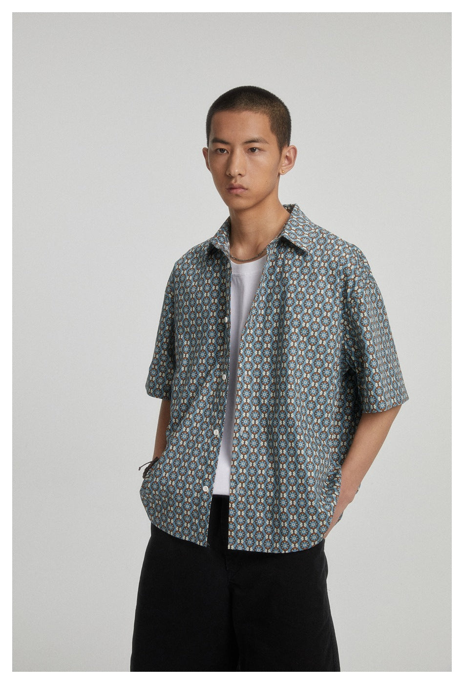 Model wearing an open blue geometric-pattern short-sleeve shirt over a white tee with black shorts.