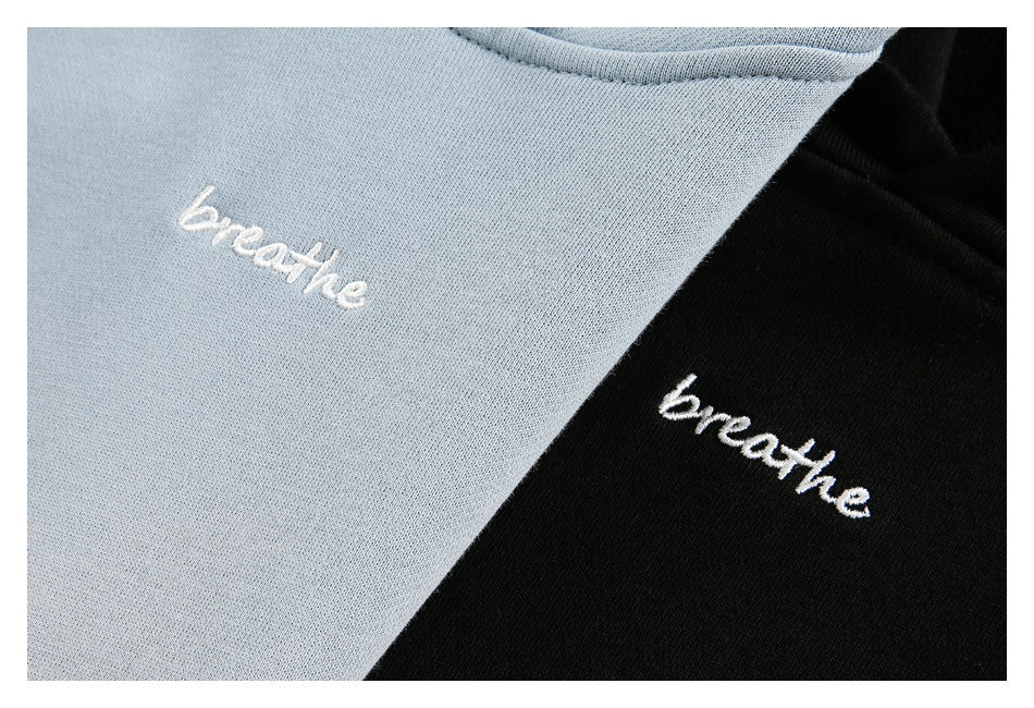 Close-up of white “breathe” embroidery on light blue and black sweatshirt fabric.