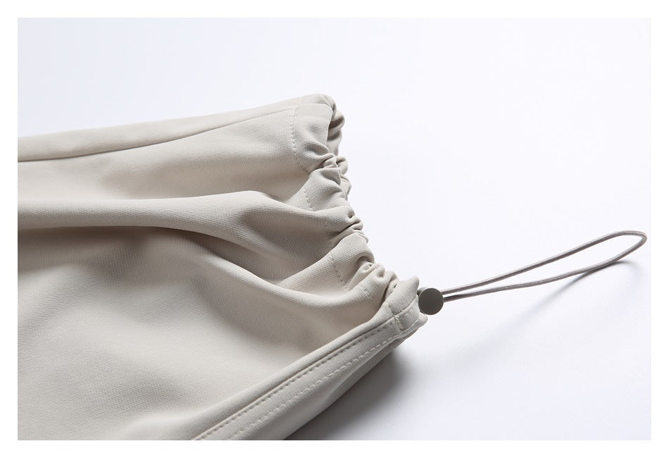 Close-up of a light beige trouser cuff with gathered elastic and an extended cord loop with stopper.