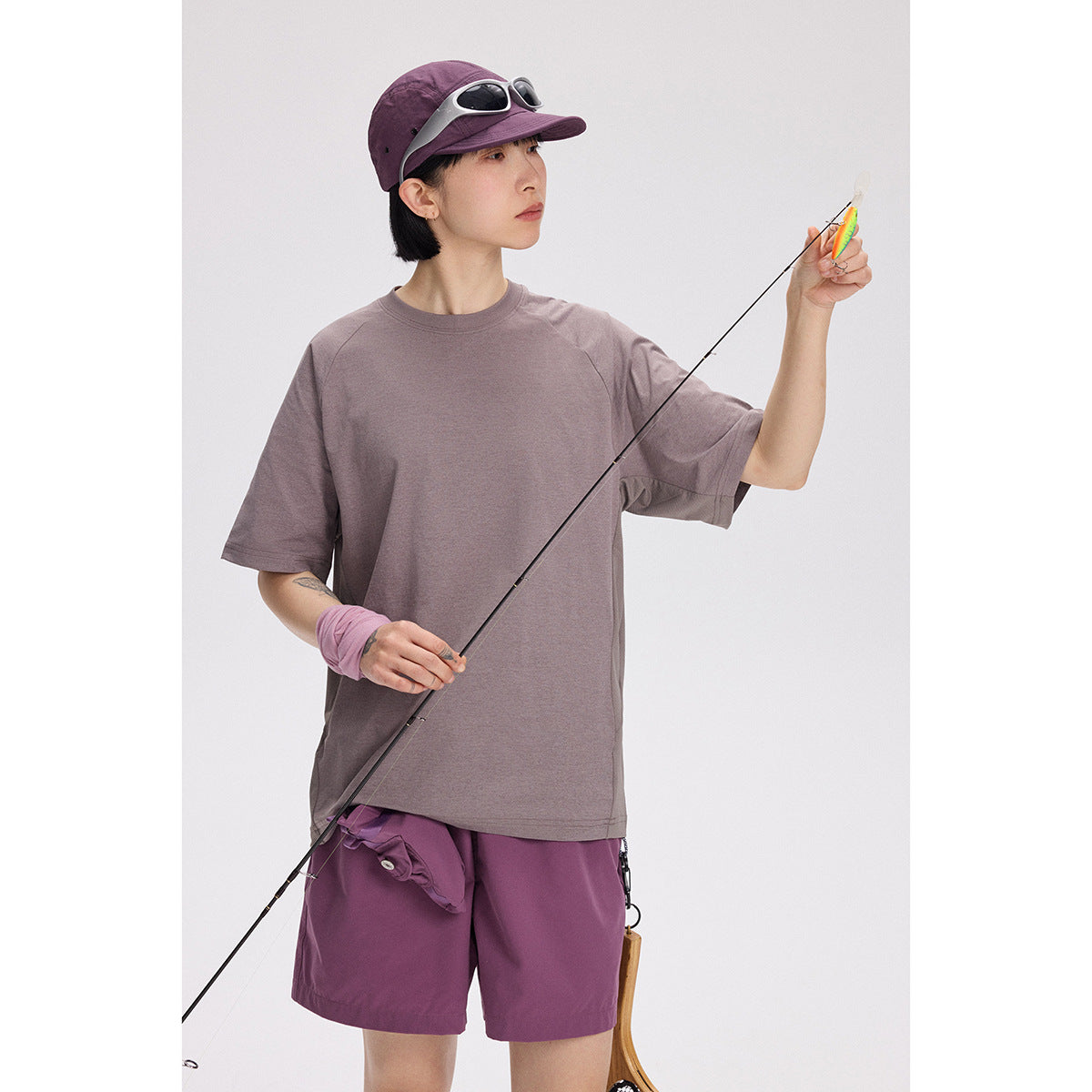 Model wearing a loose muted mauve T-shirt and plum shorts while holding a fishing rod.