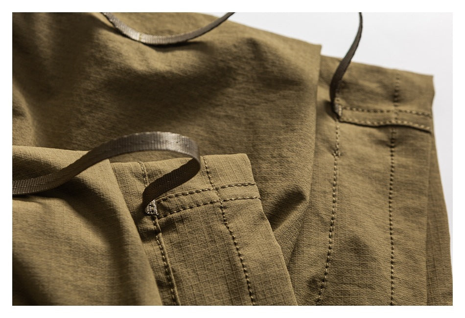 Close-up of olive-brown trousers showing stitched webbing loops and reinforced seams.
