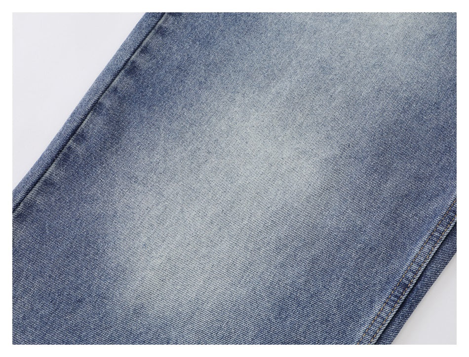 Close-up of faded blue denim fabric with a diagonal seam and tan stitching.