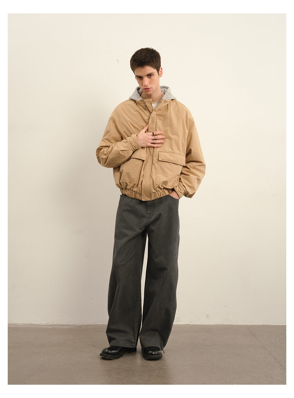 Model wearing a tan hooded jacket with large flap pockets and wide charcoal trousers.