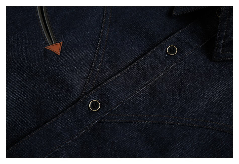 Close-up of dark indigo denim with two buttons, contrast stitching, and a brown-tipped black trim detail.