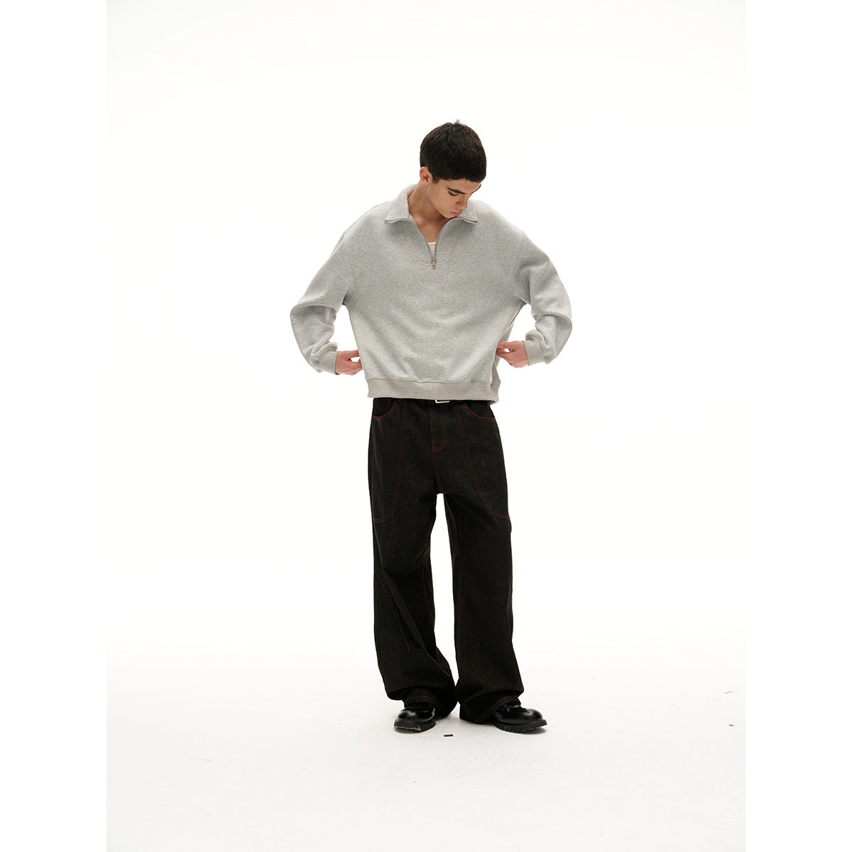 Model looking down in a light gray quarter-zip pullover and black wide-leg pants with contrast stitching.