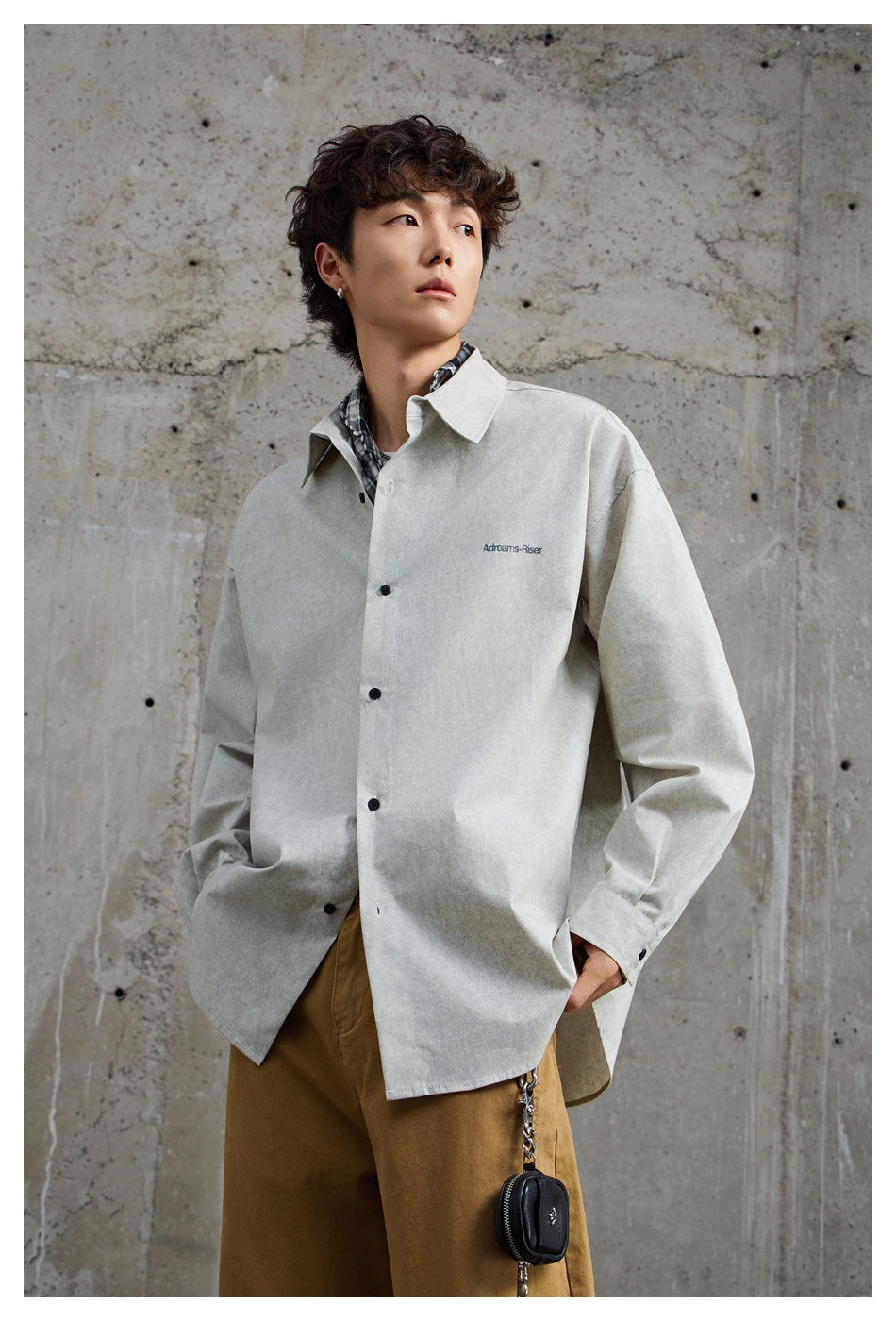 Model wearing an oversized light gray button-up shirt with black buttons and a small chest print.