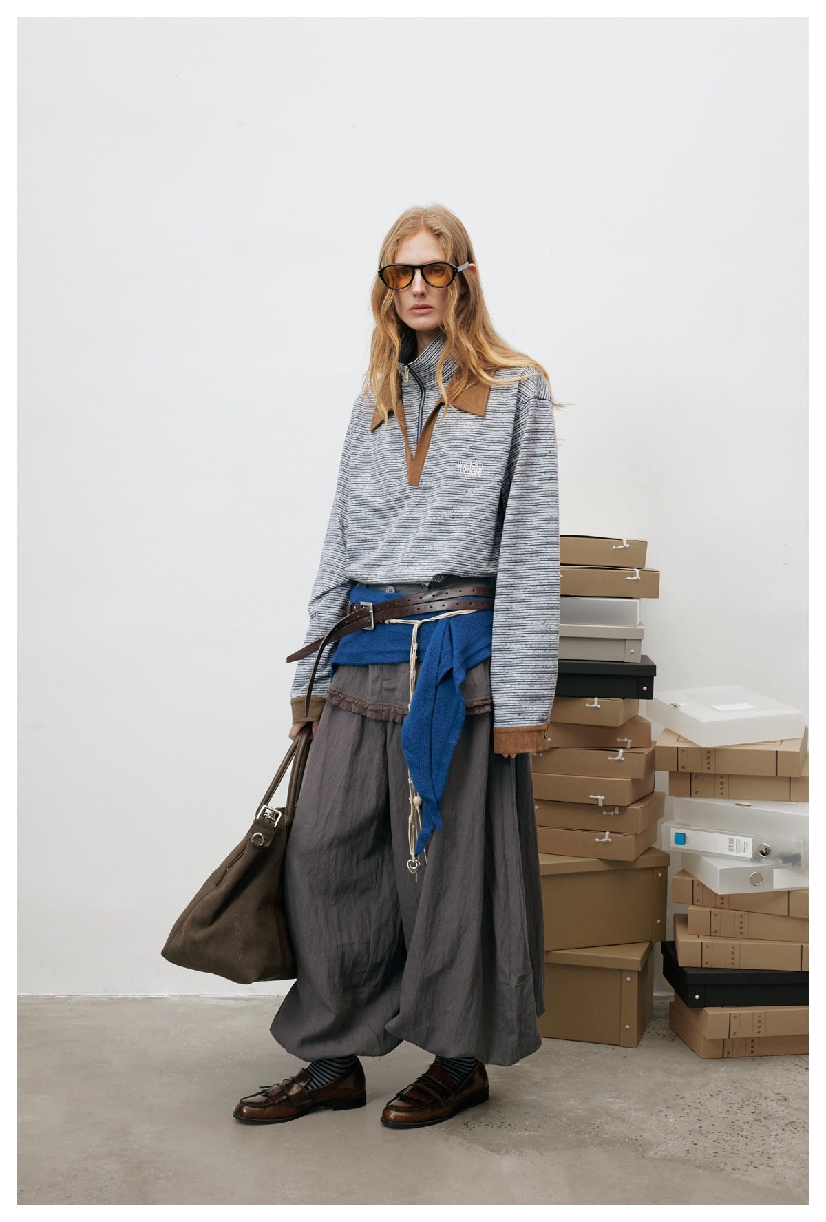 Full-length model view of the striped half-zip polo top with brown cuffs, styled with a blue scarf, belt and loafers