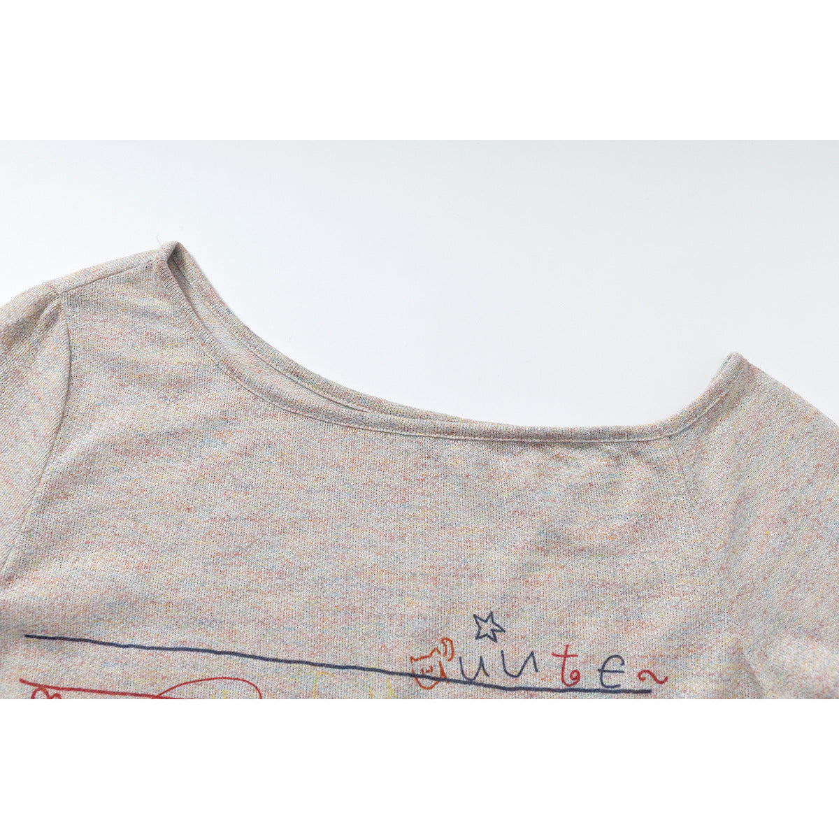 Close-up of a wide neckline on a light gray speckled top, with part of a colorful line-art print visible.