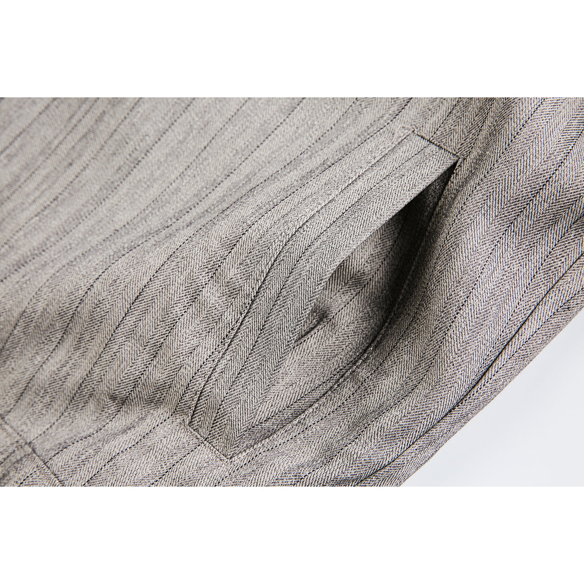 Close-up of a slanted pocket opening and seams on a light gray pinstriped jacket.
