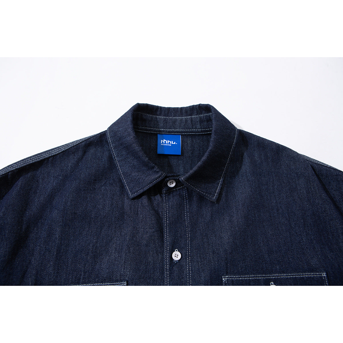 Close-up of a dark indigo button-up shirt collar, placket, and shoulder seams, with a blue neck label.