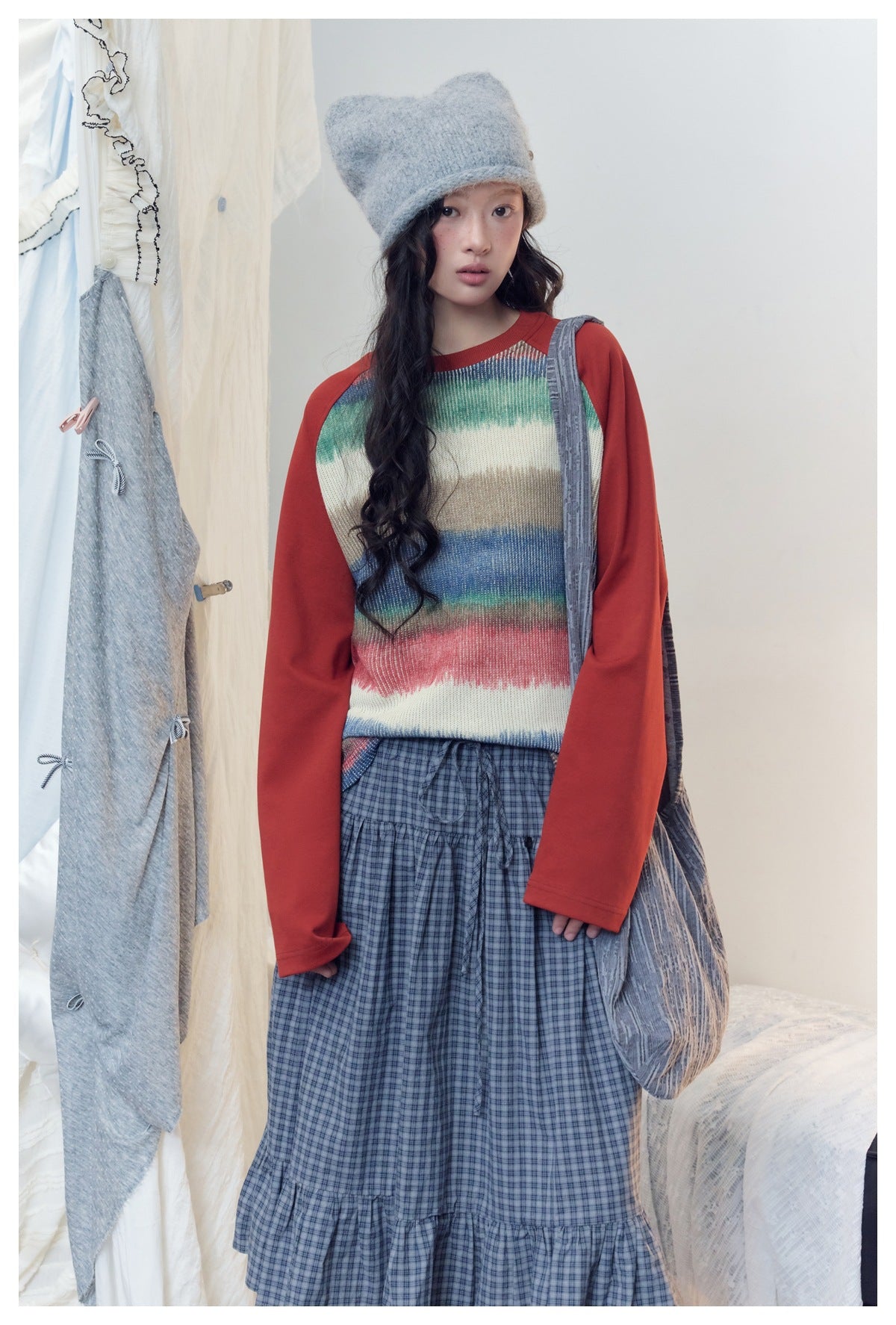 Model wearing a cream sweater with multicolor horizontal stripes, red raglan sleeves and a blue plaid tiered skirt.