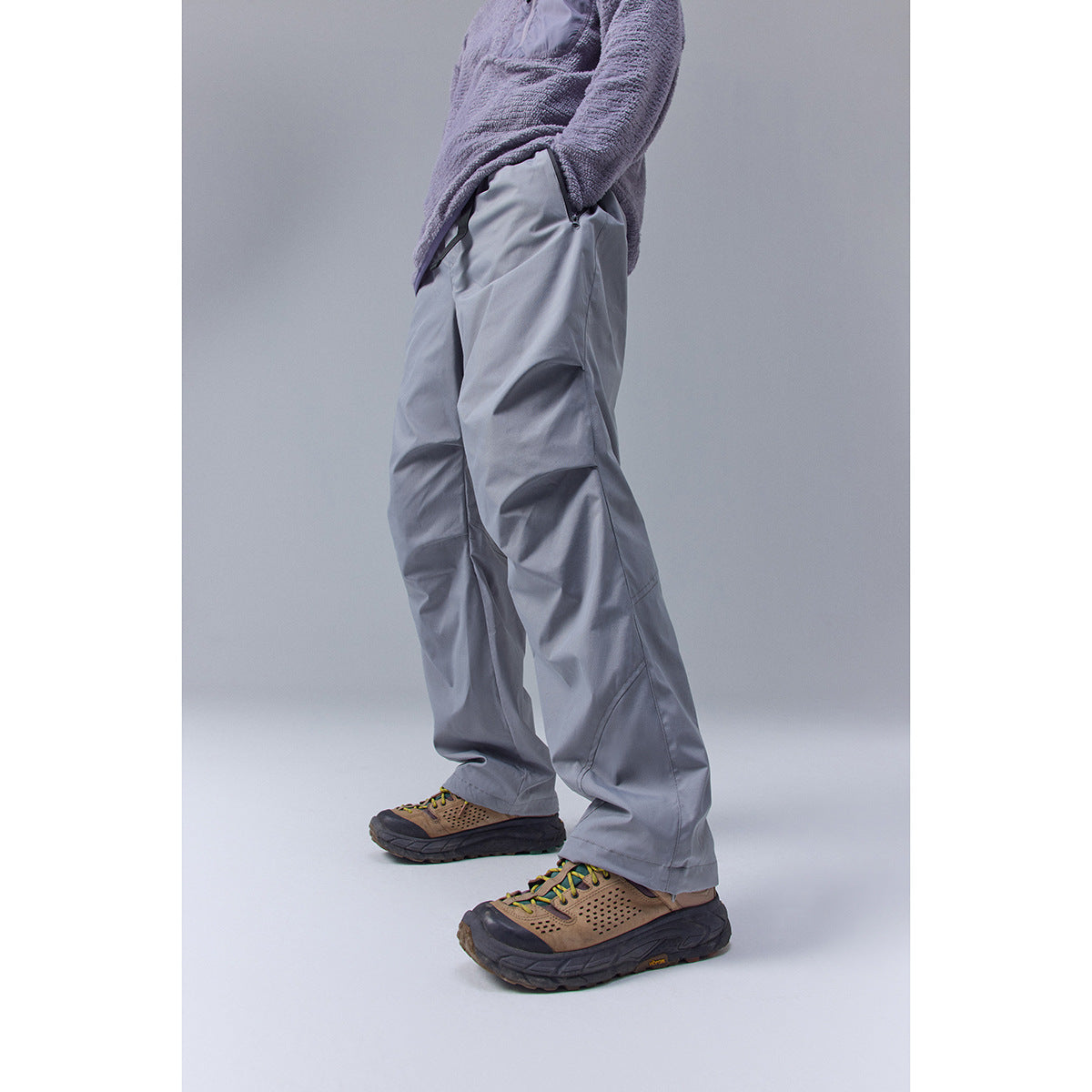 Model wearing gray wide-leg pants with a purple fleece-style top and tan hiking shoes, cropped side view