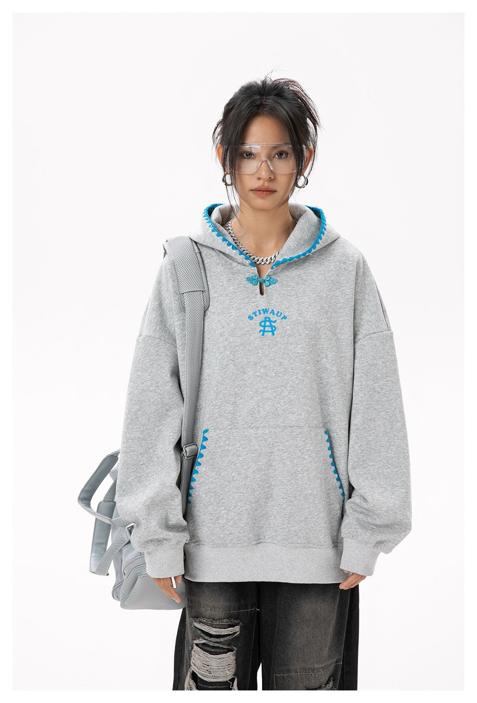 Model in a gray oversized hoodie with blue trim and kangaroo pocket, shown with a gray shoulder bag.