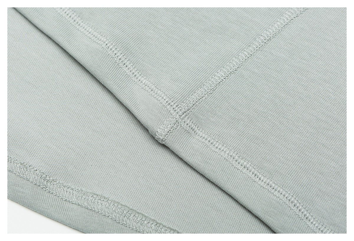 Close-up of intersecting stitched seams on pale sage-gray knit fabric.