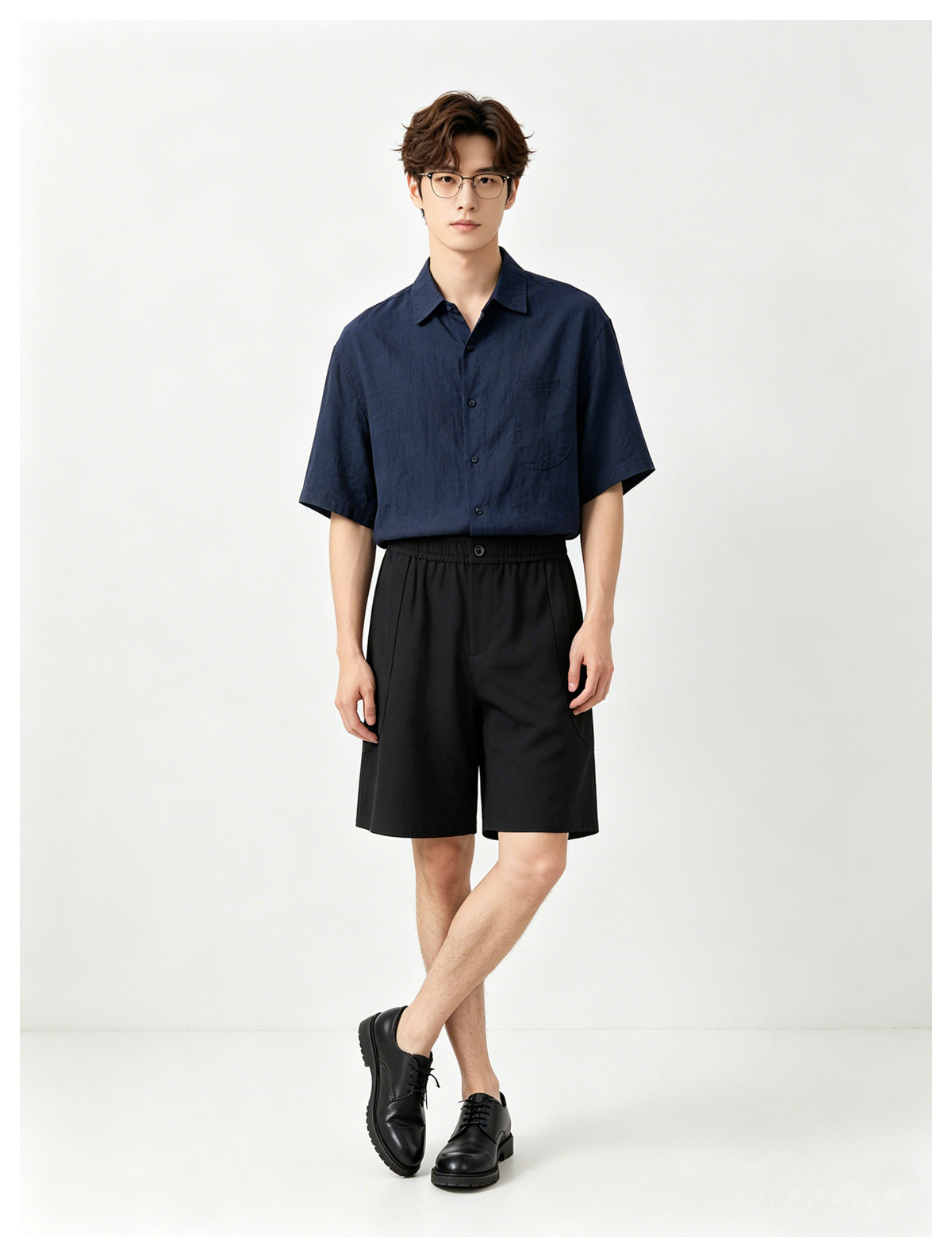 Model standing in black wide-leg knee-length shorts with elastic waist, navy shirt and black derby shoes