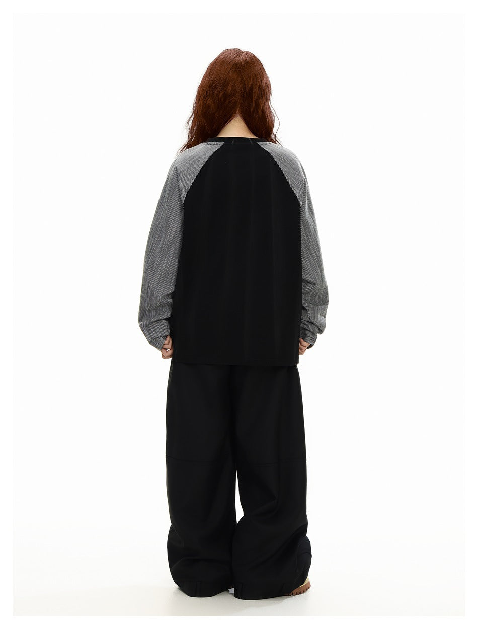 Rear view of a model wearing a black top with gray pinstriped raglan sleeves and wide black pants.
