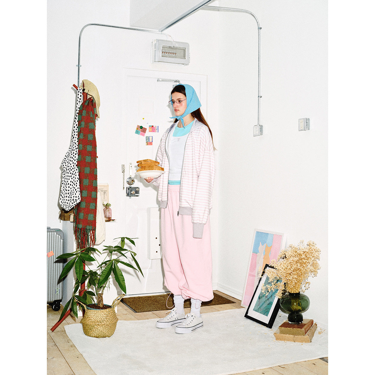 A model wears an open pale pink-and-white striped zip hoodie with gray trim and loose pink pants.