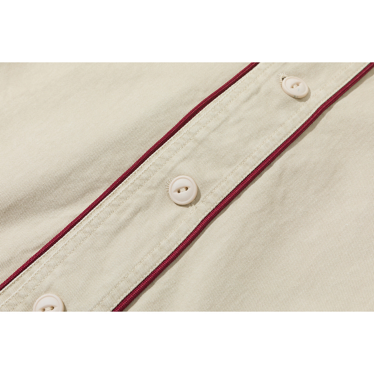 Close-up of a cream shirt placket with burgundy piping and three cream buttons.