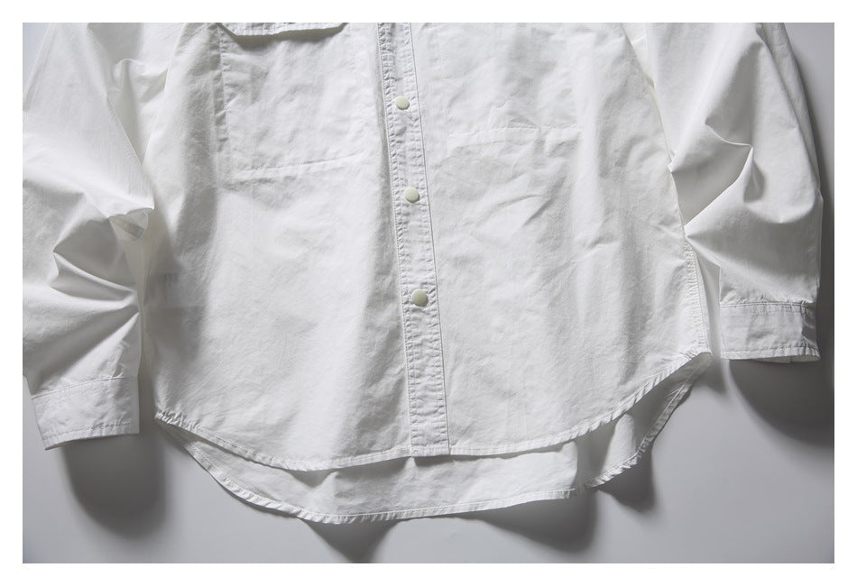 White long-sleeve button-front shirt laid flat, showing a chest pocket, snap buttons, and a curved hem.