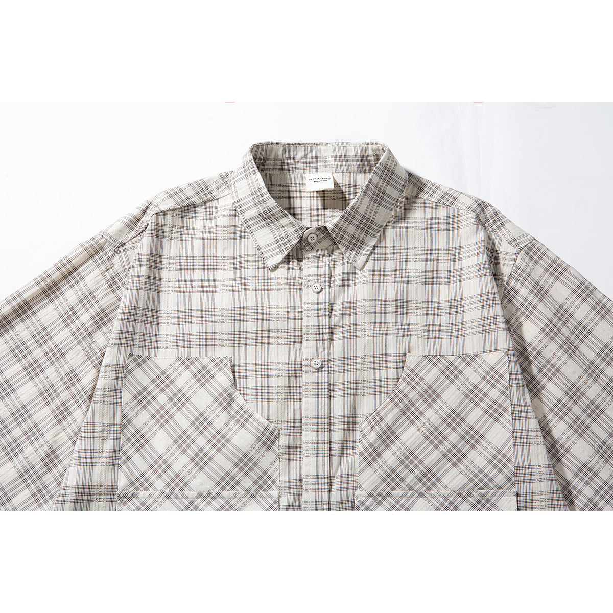 Close-up of an off-white plaid short-sleeve button-up shirt, showing its collar, buttons, and large chest pockets.