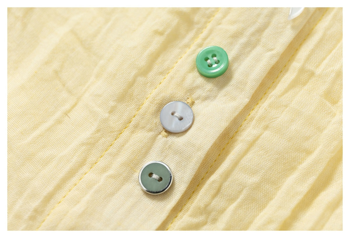 Close-up of three green, pearly white, and gray buttons on the crinkled pale yellow shirt fabric.