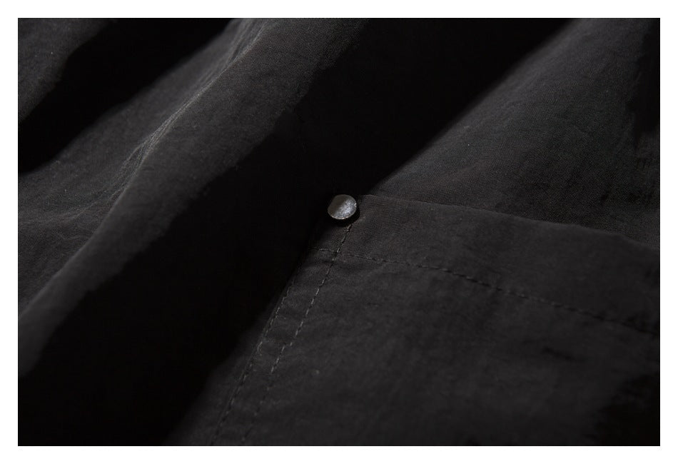 Close-up of black shorts fabric and a metal snap at the corner of a stitched pocket.