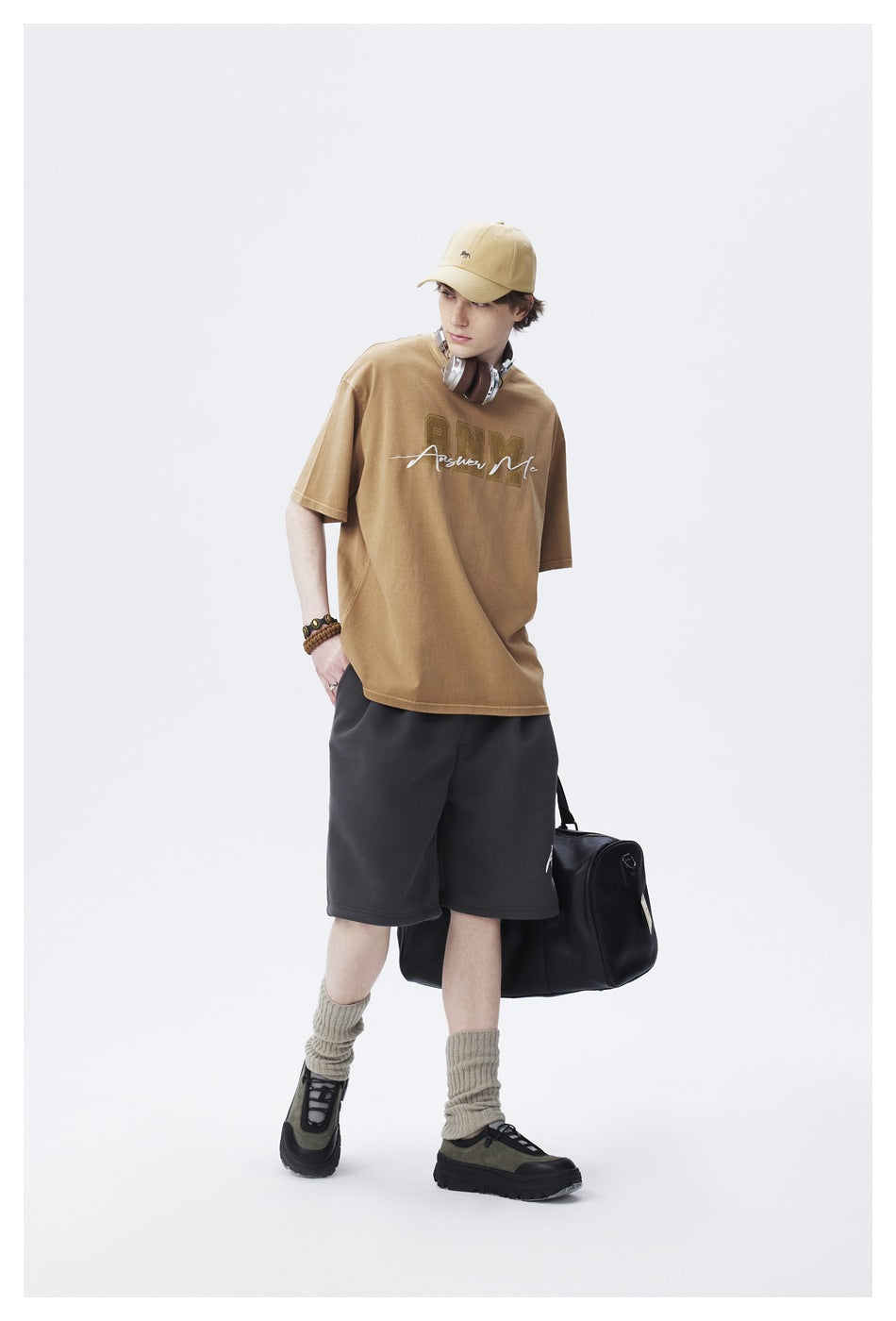 Model wearing a tan graphic T-shirt and charcoal shorts, shown in a relaxed standing pose.