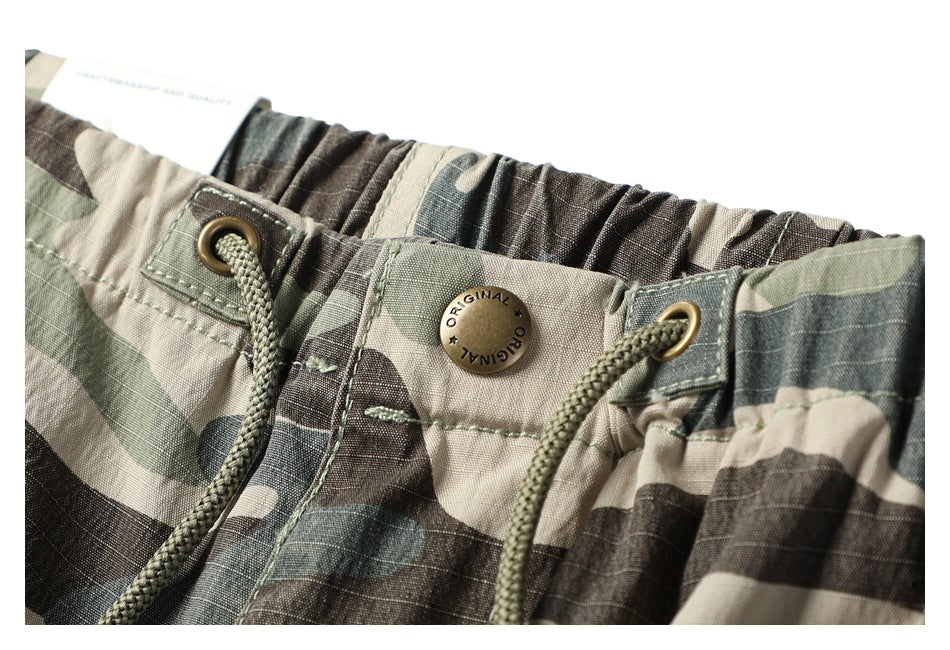 Close-up of the camouflage trousers' gathered waistband, drawcord eyelets and metal waist button.