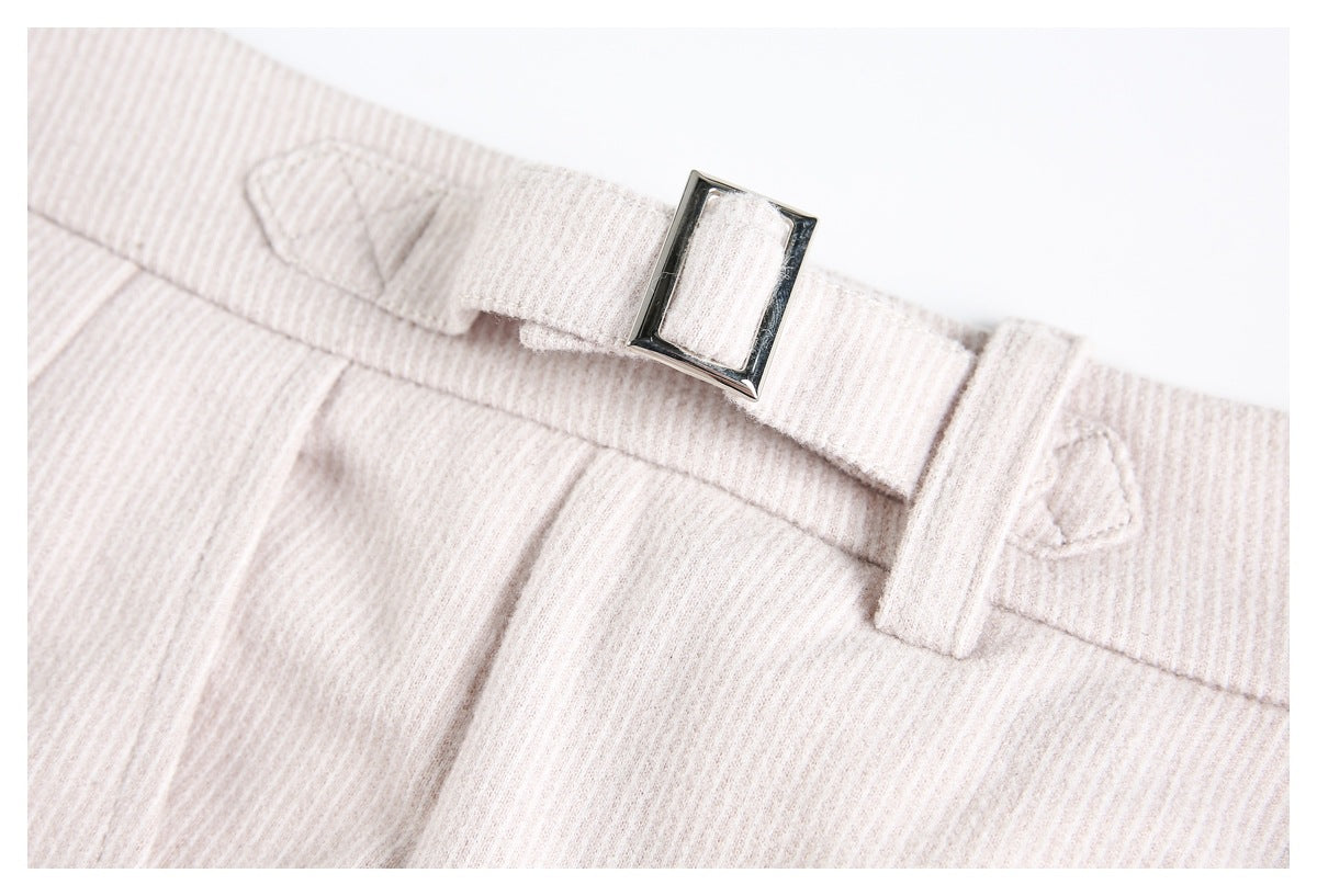 Close-up of the waistband, belt loops, and rectangular metal buckle on pale beige ribbed trousers.