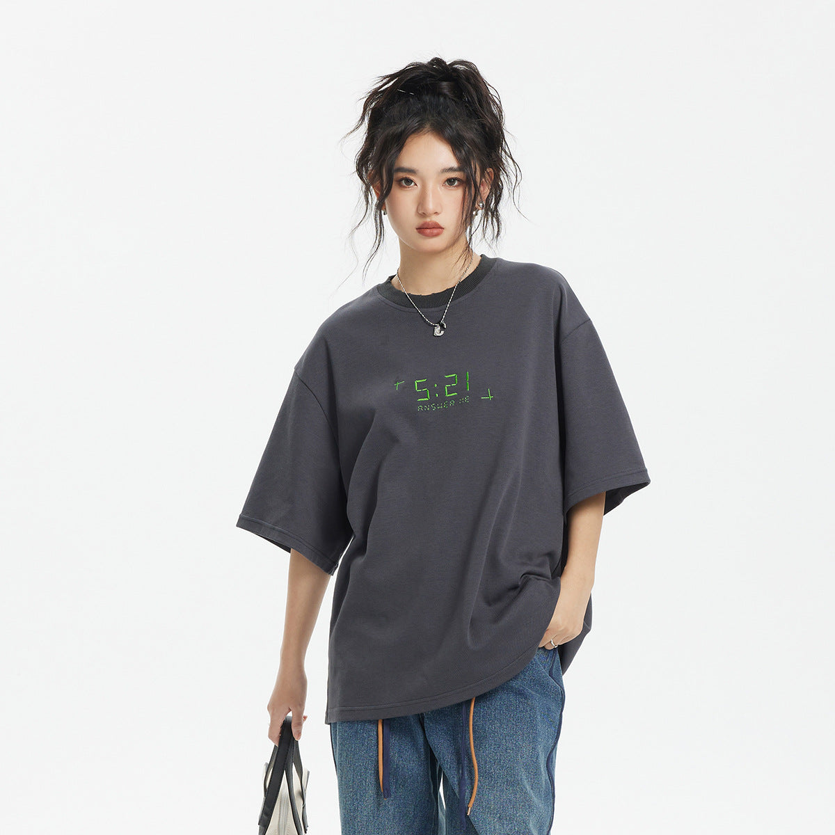 Model wearing an oversized charcoal gray T-shirt with small green chest lettering and blue jeans.
