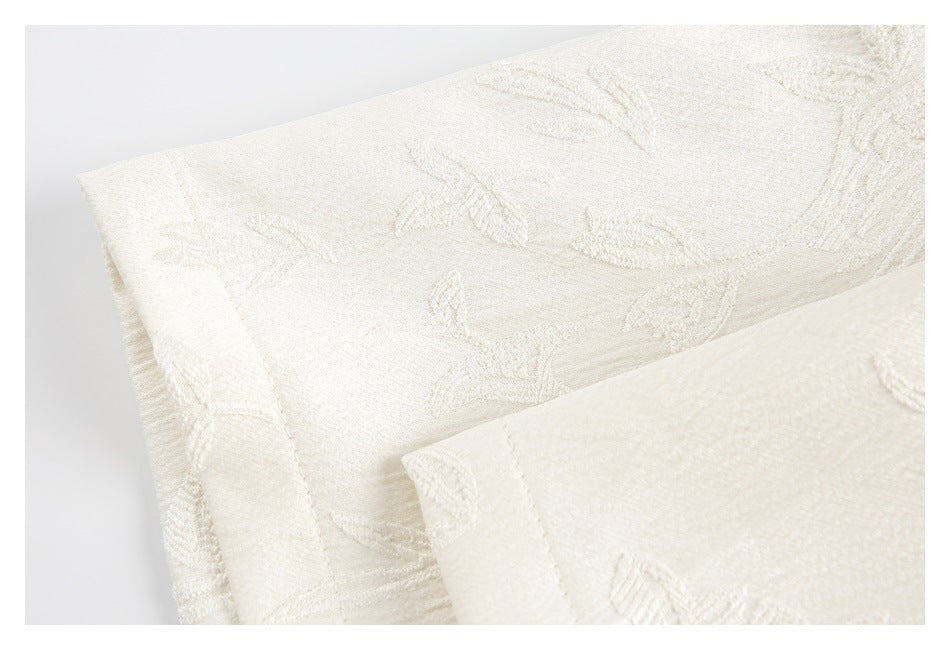 Close-up of folded ivory garment edges with subtle raised floral patterns.