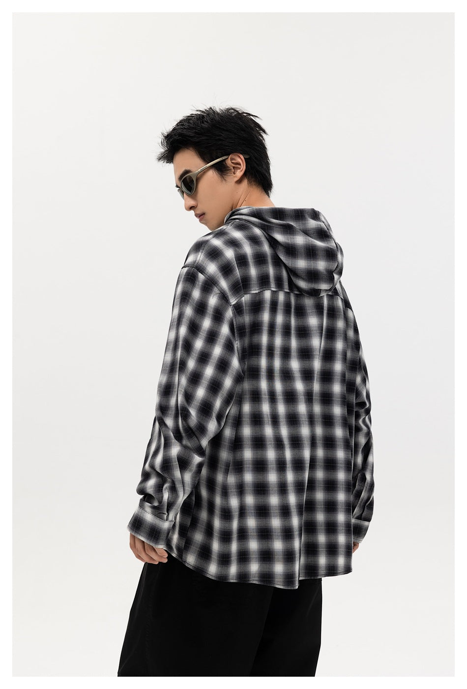 Back view of a model wearing a black-and-white plaid hooded button-up shirt with loose black pants.