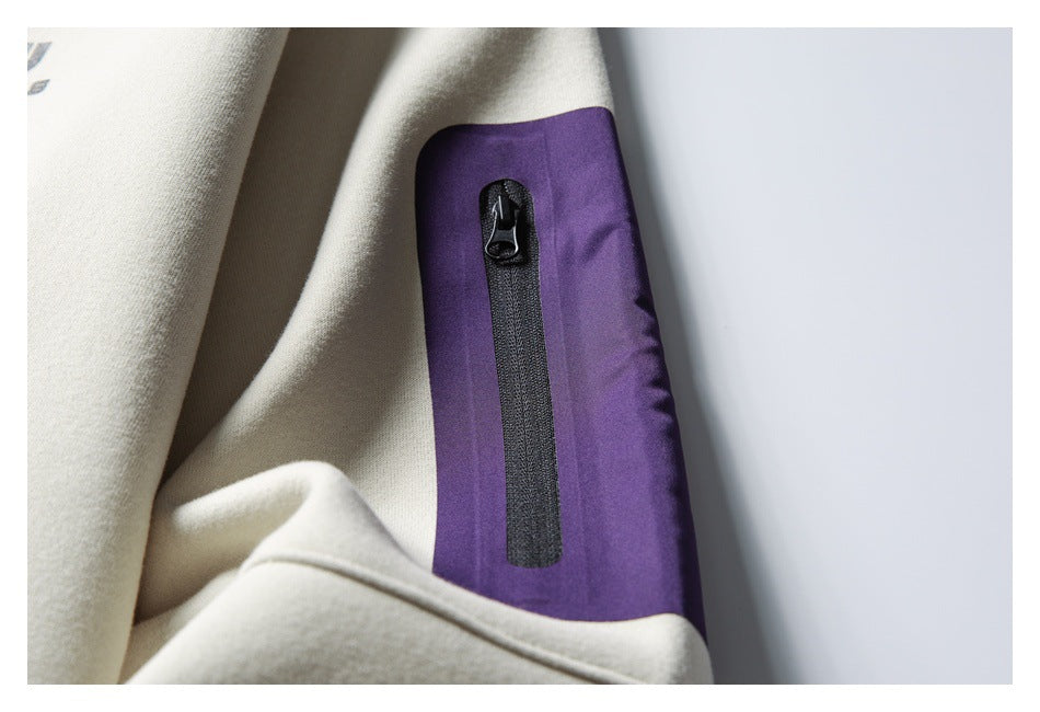 Close-up of a cream sweatshirt sleeve with a purple zip pocket panel and black zipper.