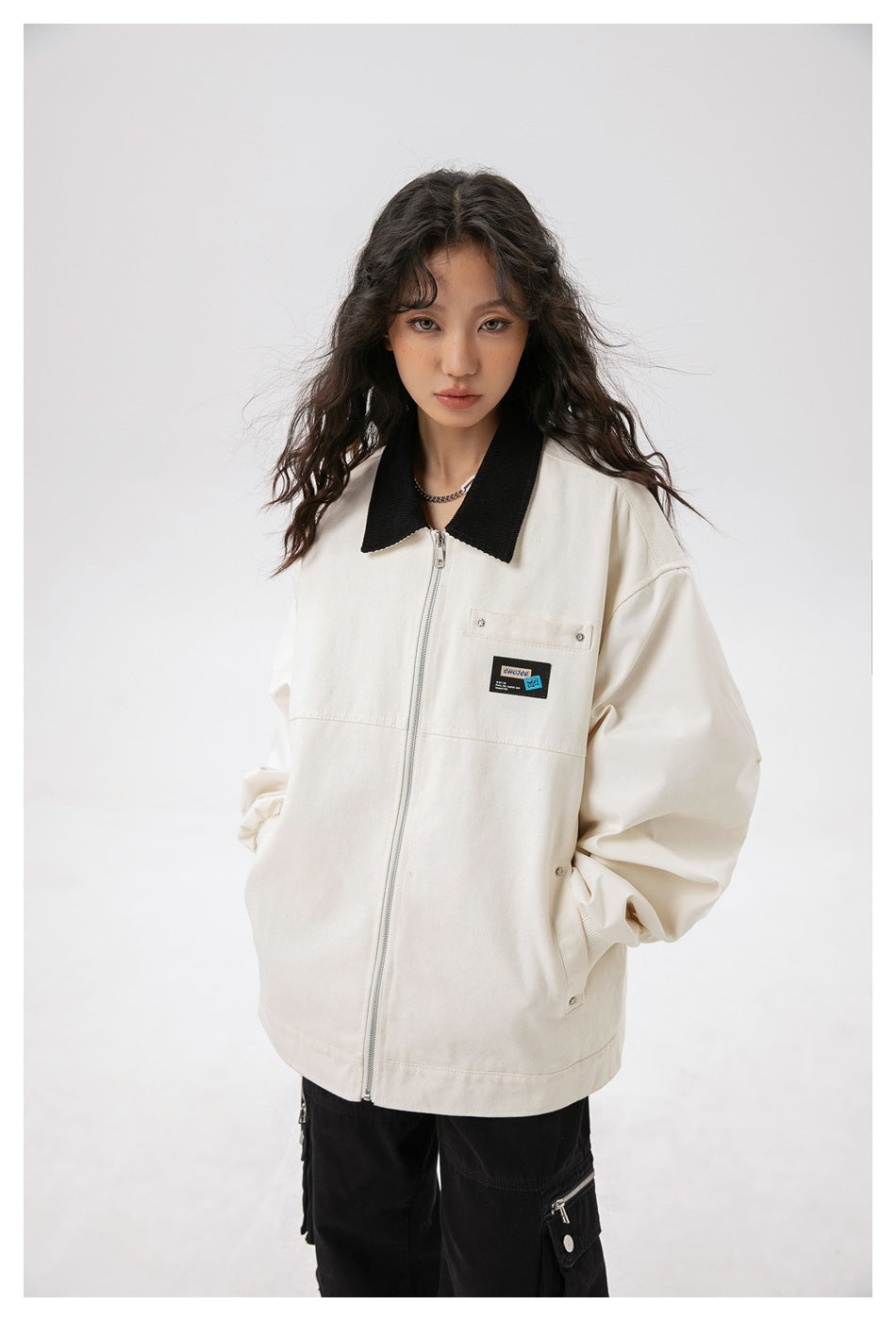 Closer front view of an ivory jacket with a black collar, silver zipper, chest pocket, and small patch.