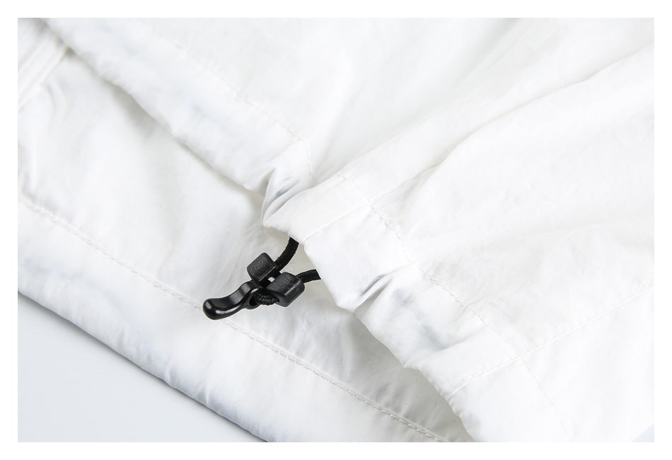 Close-up of a black cord toggle at a seam on white fabric.