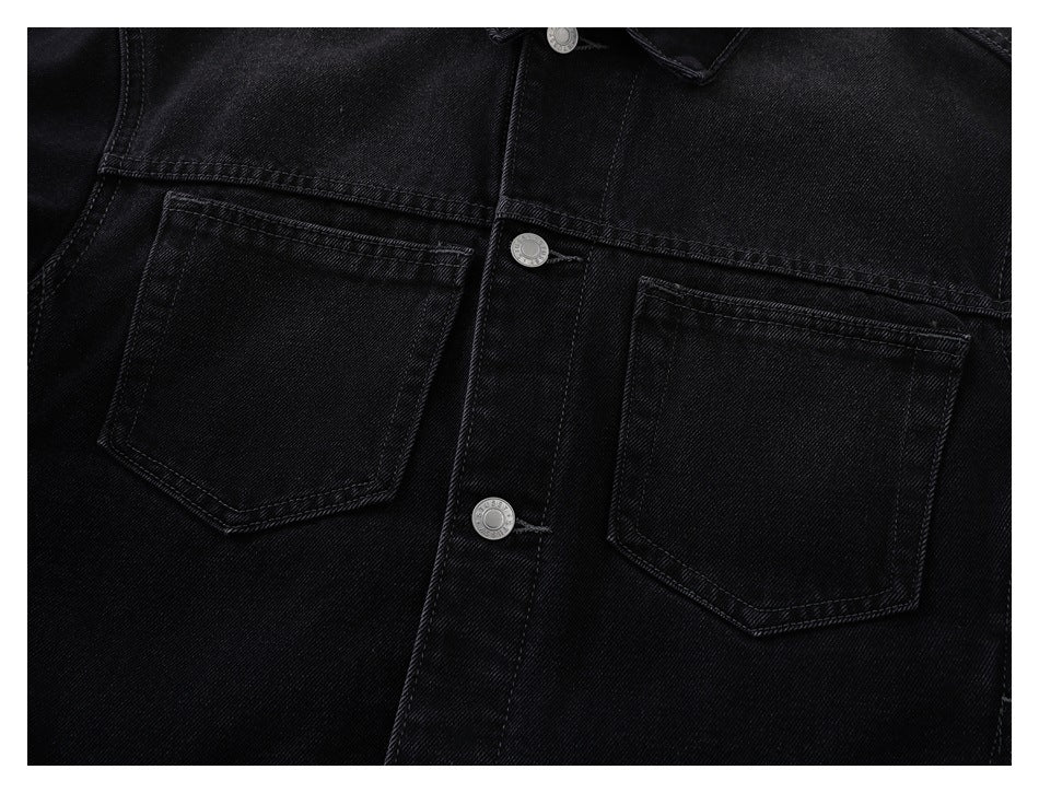 Close-up of a black denim jacket front with two chest pockets and silver snap buttons.