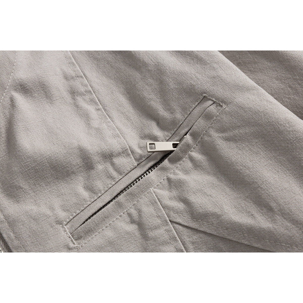 Close-up of a light gray jacket's diagonal zip pocket and metal zipper pull.