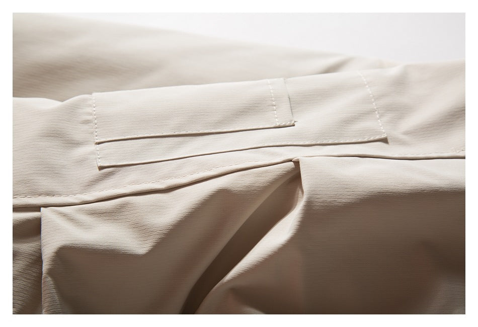 Close-up of a light beige garment showing a stitched rectangular flap and layered seams.